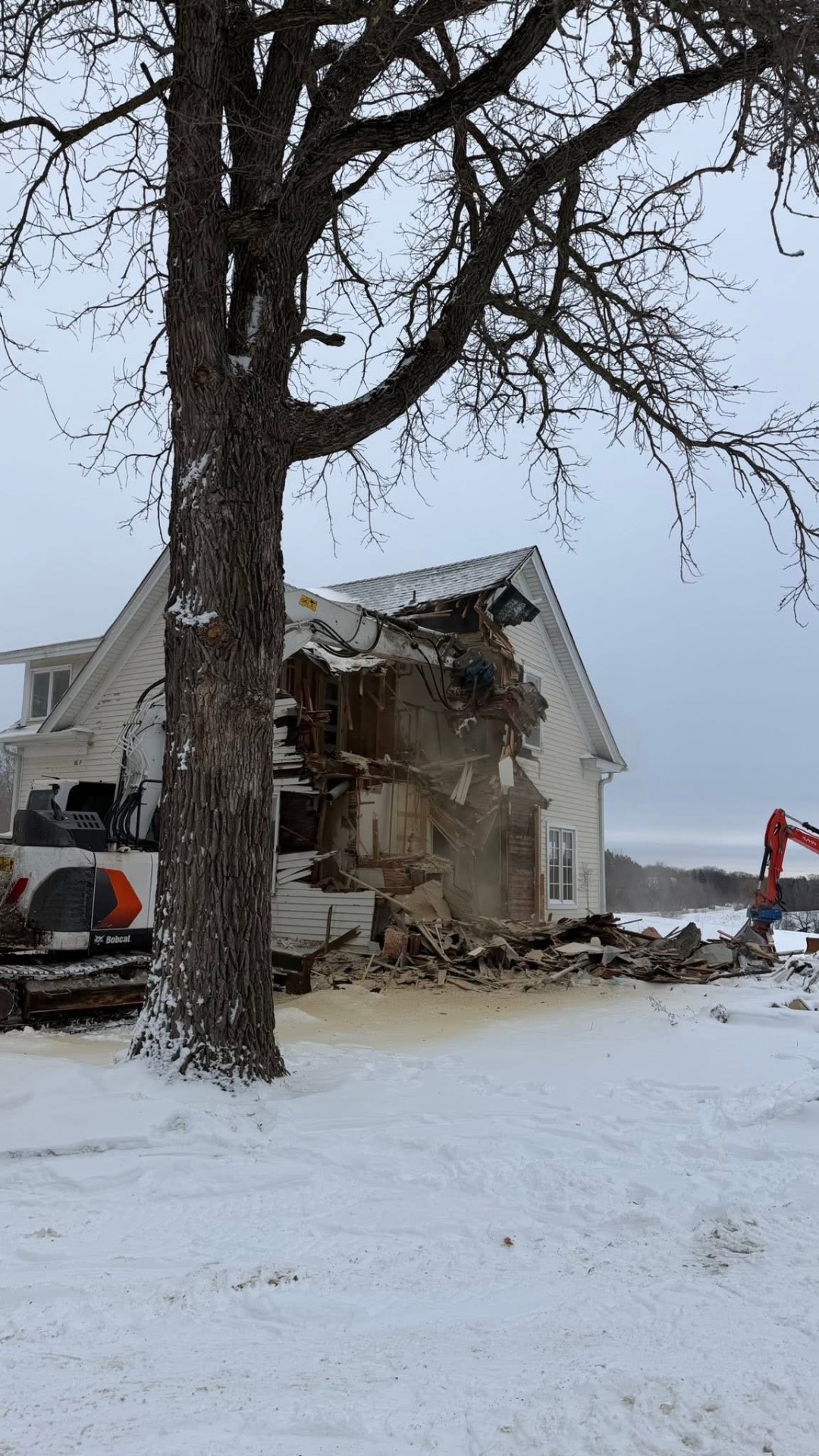 Bobcat excavator tearing down farmhouse in winter